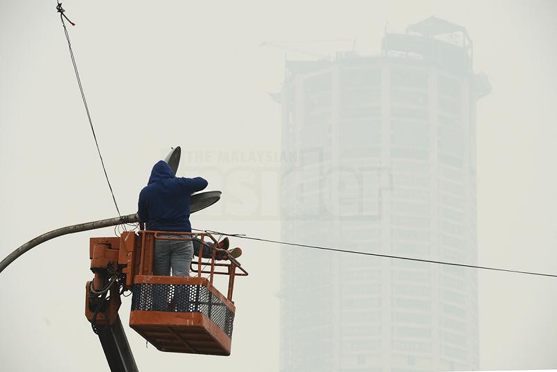 Workers repairing a street lamp are seen against a smoky backdrop of Komtar in George Town, Penang. Schools in various states will remain closed tomorrow for a straight fourth day‎, after the API levels continue to hover over the unhealthy or very unhealthy levels. – The Malaysian Insider pic by Hasnoor Hussain, October 21, 2015.